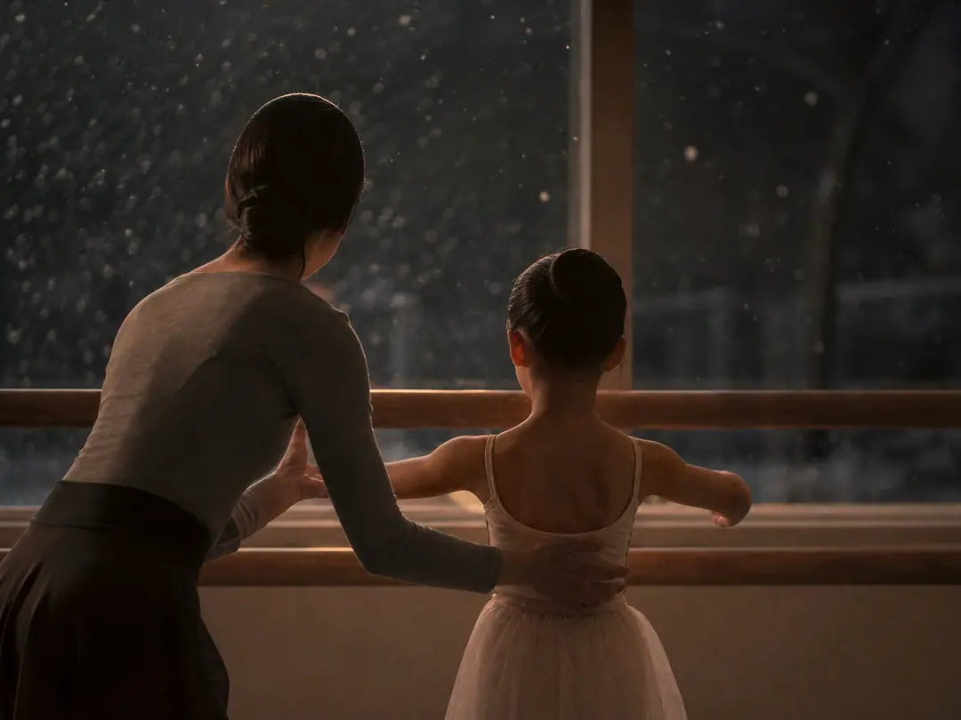 雪の夜のスタジオで、先生が少女の腕をそっと導く後ろ姿